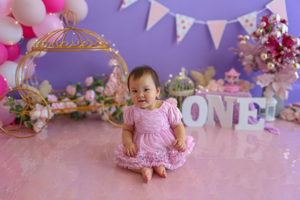 Newborn girl in a pink and purple themed cake smash. princess carriage in the background bringing a princess feel to the whole shoot.