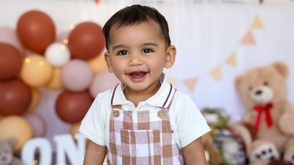 Cake smash for a baby boy enjoying a teddy bear themed cake smash. Happy smiling baby.