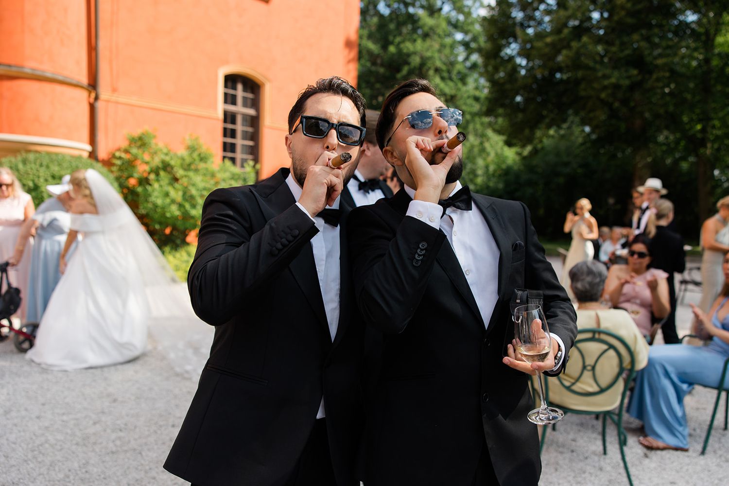 Groomsmen in black tuxedos and sunglasses pose together outdoors during a wedding celebration.