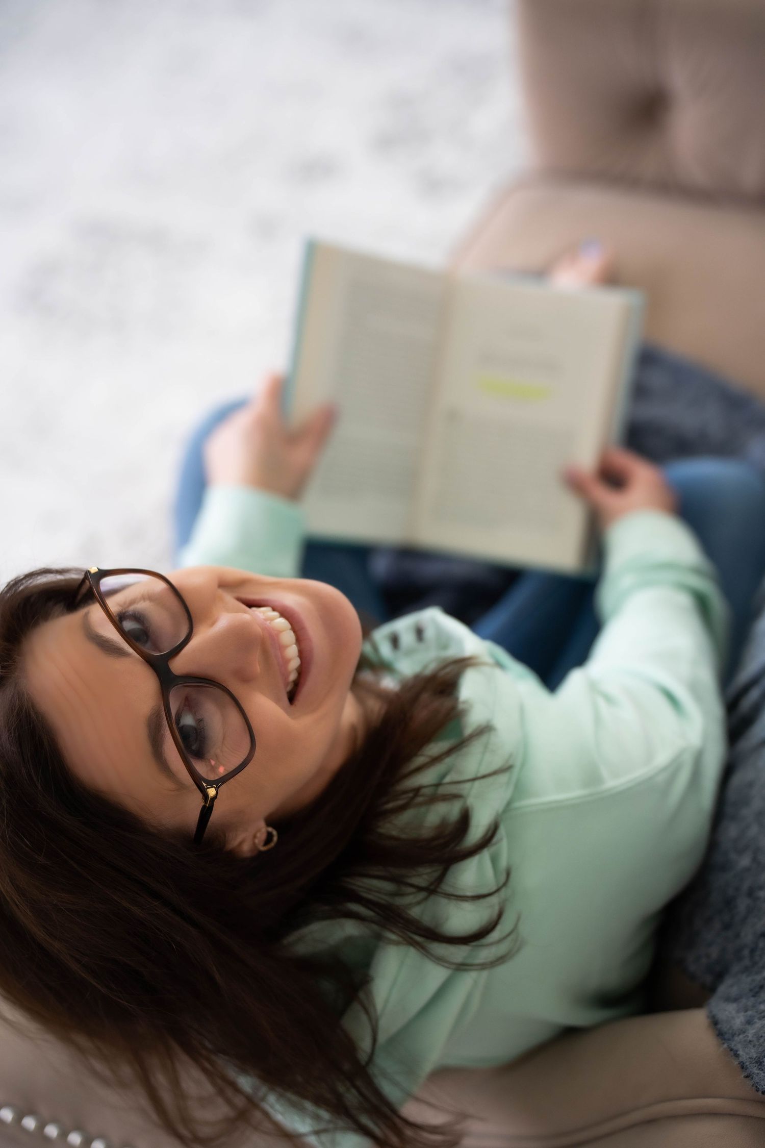 Person with glasses reading while lying down on a couch.