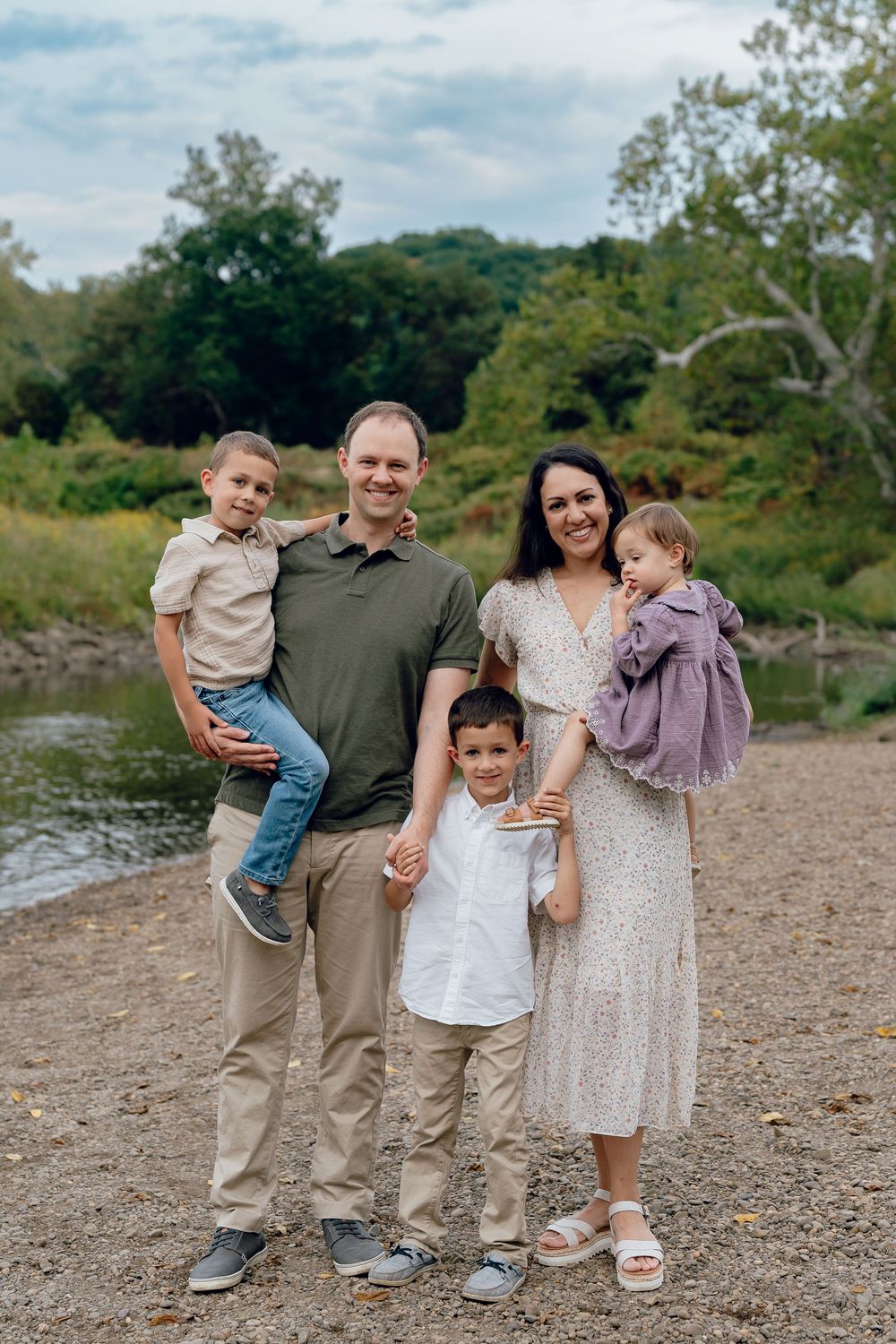 Family of five stands together on rocky riverbank during outdoor photo session in natural setting of Cascade Valley Metro Park, Akron, Ohio