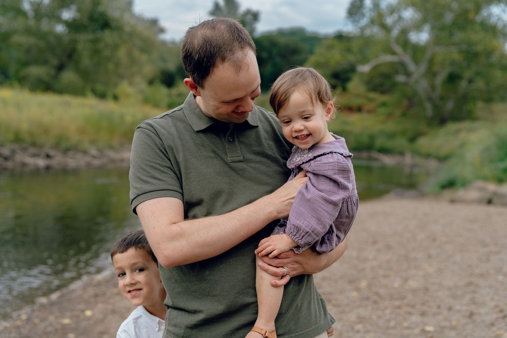 A family enjoying a sunny day together outdoors near a river with trees in Akron, Ohio Cascade Valley Metro Park Family Photo Session