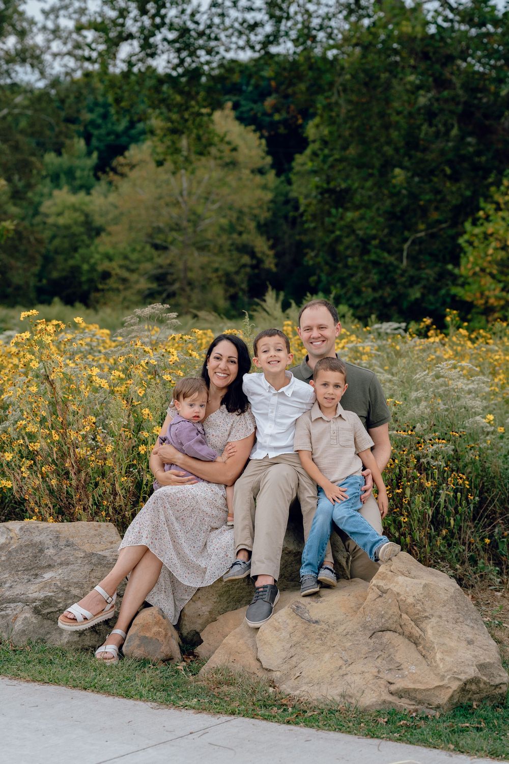 A family sits together on a large rock formation surrounded by wildflowers and greenery on a sunny day in Akron, Ohio Metro Park Family Sesh