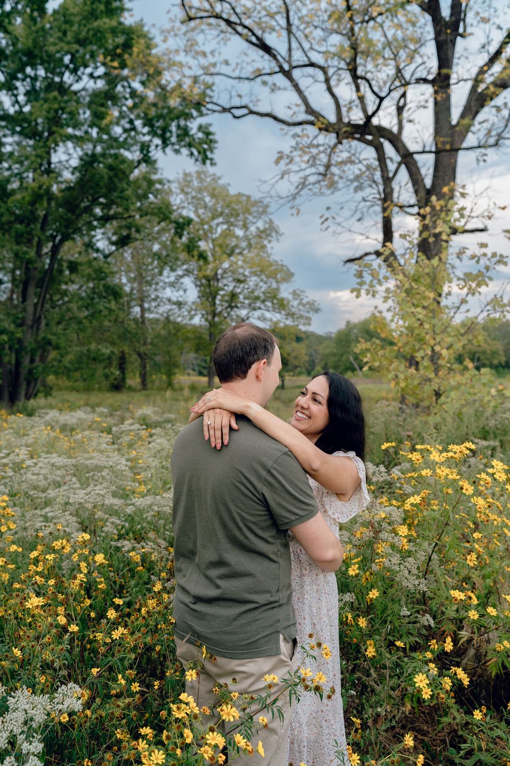 A couple embraces in a meadow surrounded by blooming yellow wildflowers and trees in Akron, OH Cascade Valley Metro Park Family Photo Sessio