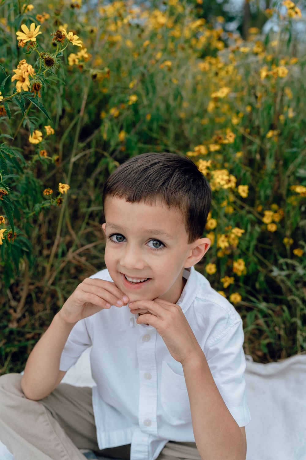 A young child poses in a white button-down shirt against a backdrop of vibrant yellow wildflowers in a garden setting for Family Photos Ohio