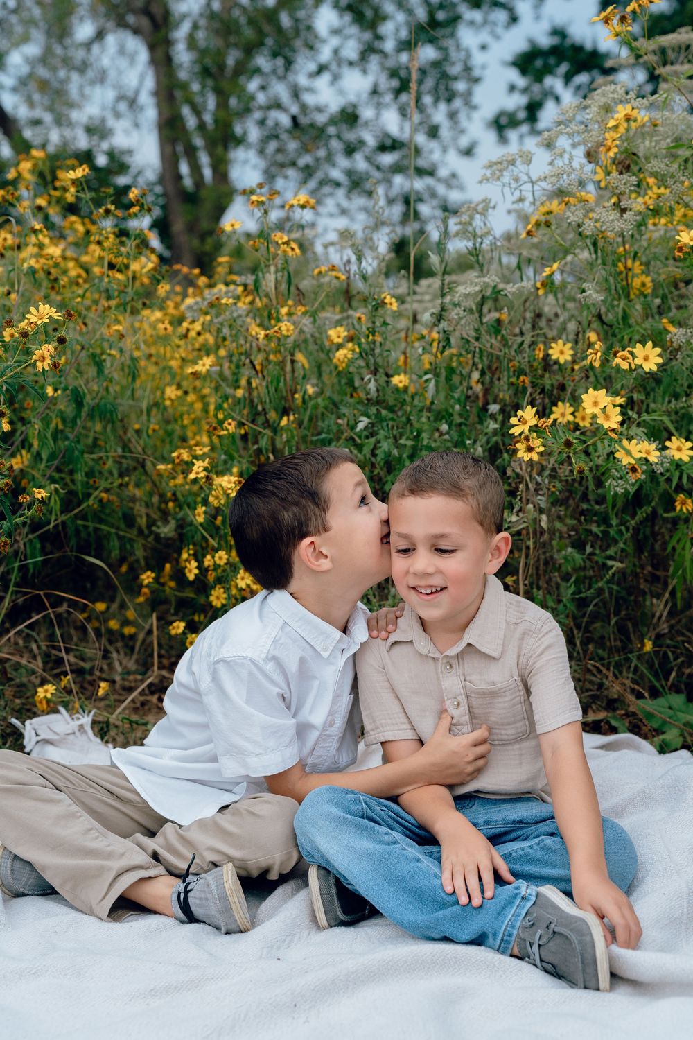 Two children sit on a white blanket surrounded by blooming yellow wildflowers in a garden at Cascade Valley Metro Park in Akron, OH Fam Pics
