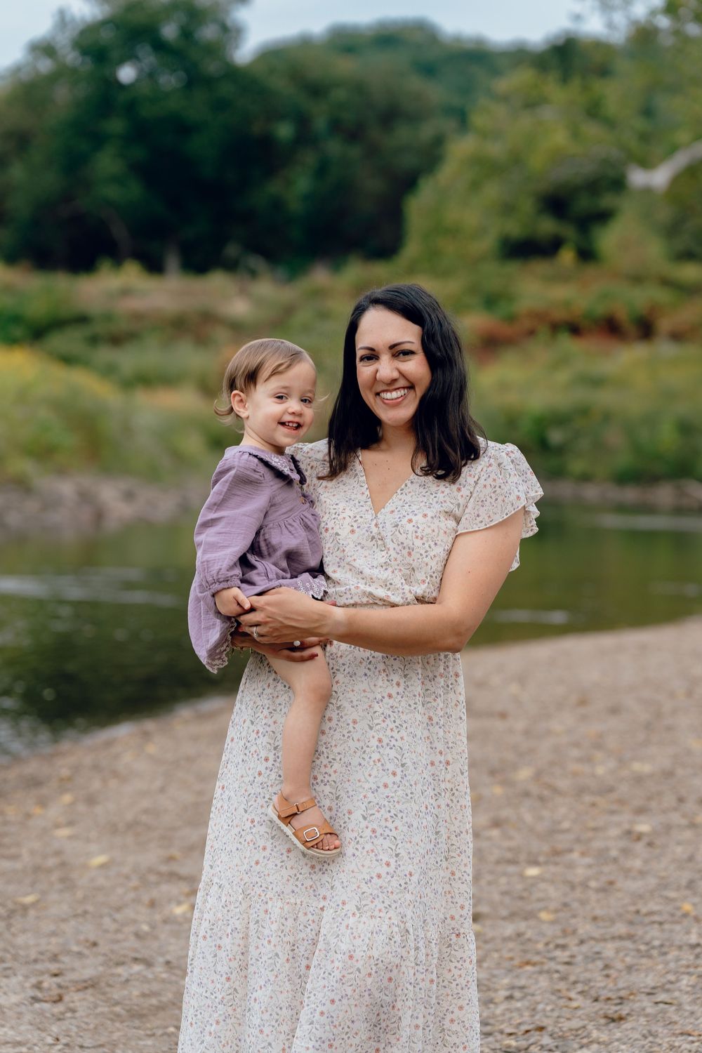 A mother and child in matching white dresses share tender moments by a riverbank at Akron, Ohio Cascade Valley Metro Park Family Photos