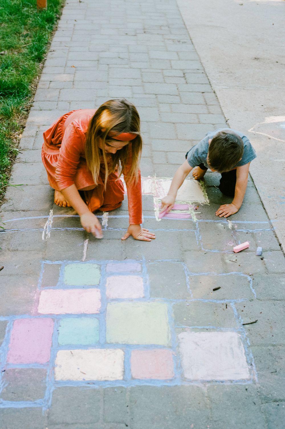 Two people drawing with colorful chalk on a concrete sidewalk on a sunny day.