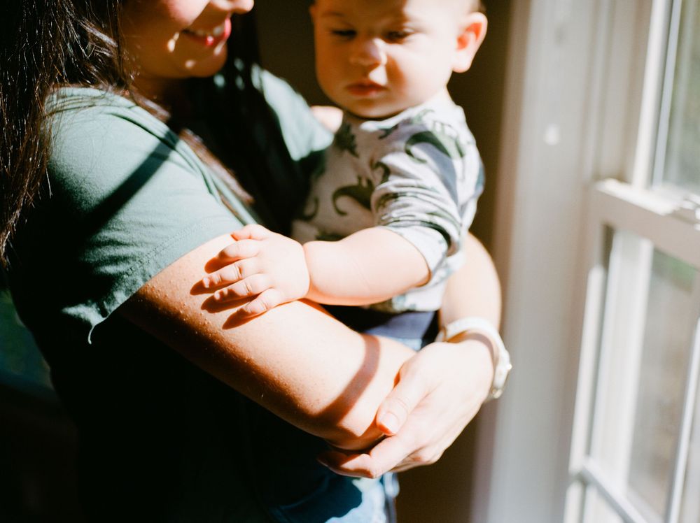A parent and child sit together reading a book near a bright window in a cozy home setting.