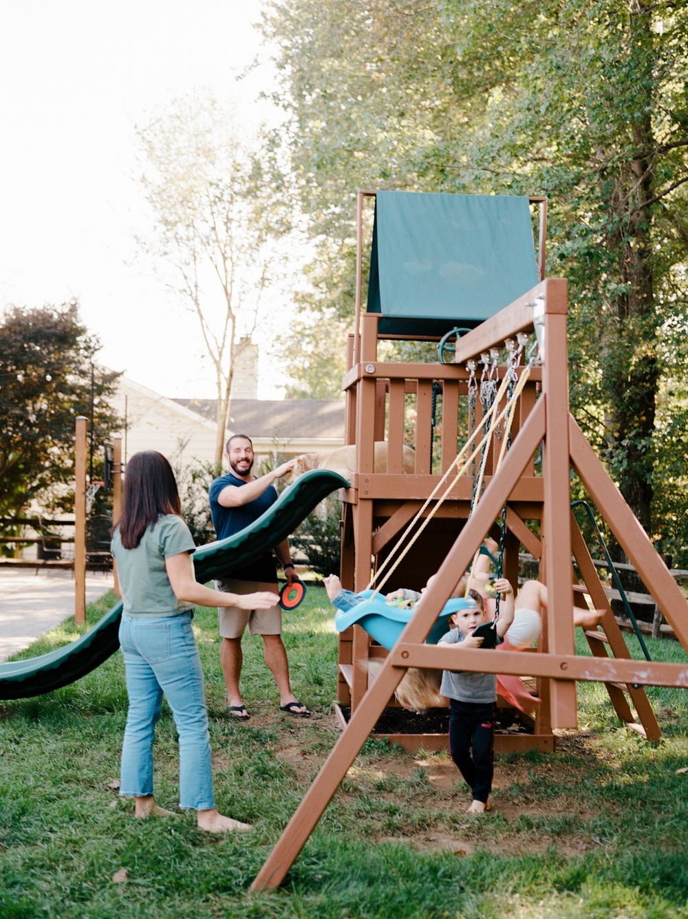 Four sequential photos show someone playing and swinging on an outdoor wooden playground set in a backyard setting.