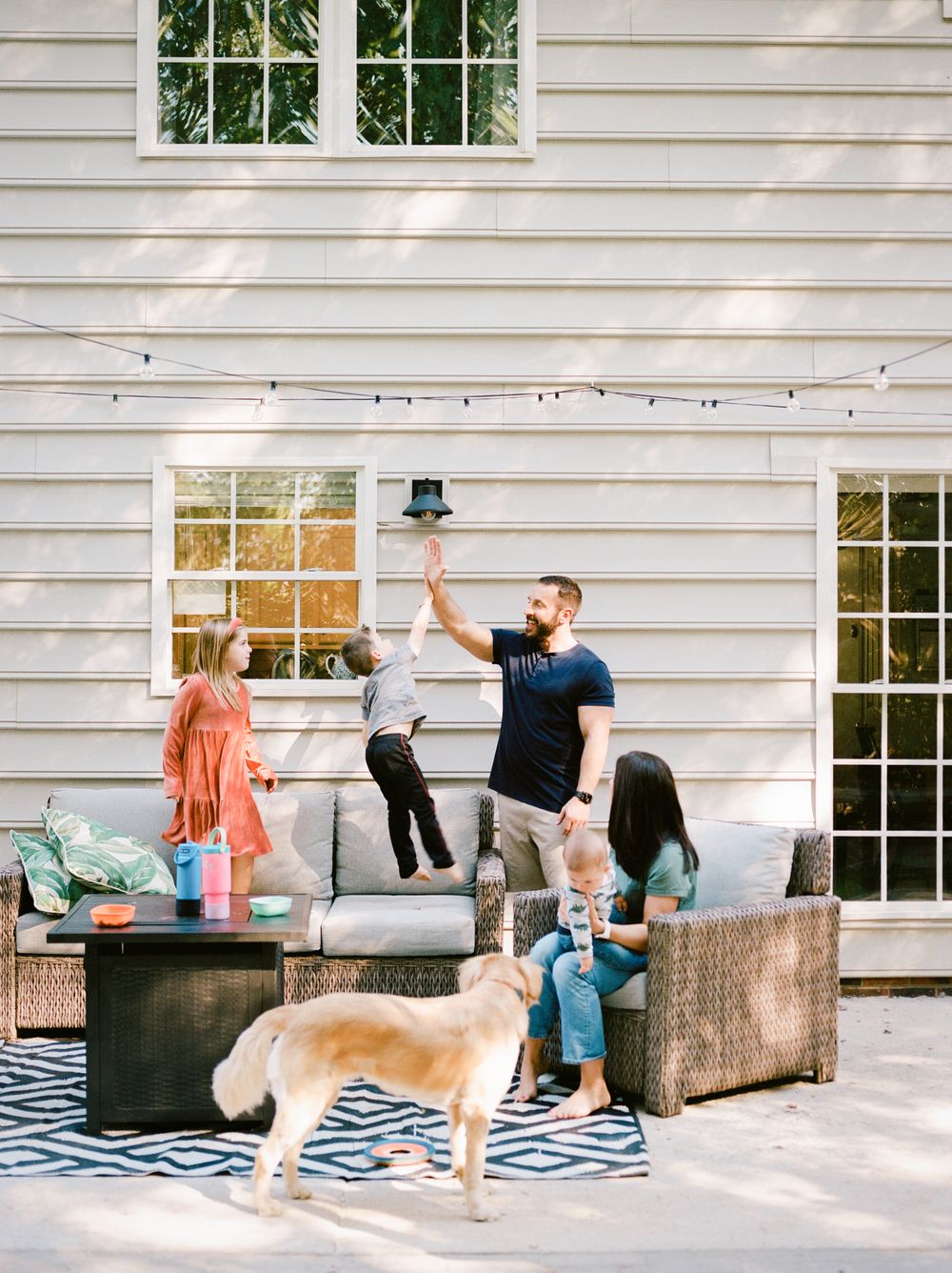 A playful sequence of a dog chasing a ball across a patio with outdoor furniture and white siding in the background.