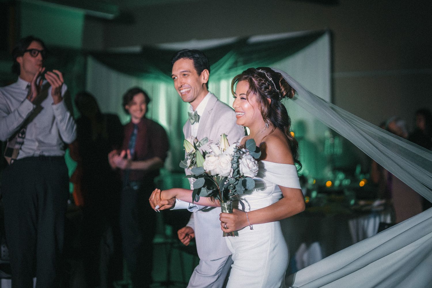 A couple shares a joyful moment dancing together at their wedding reception with green ambient lighting in the background.
