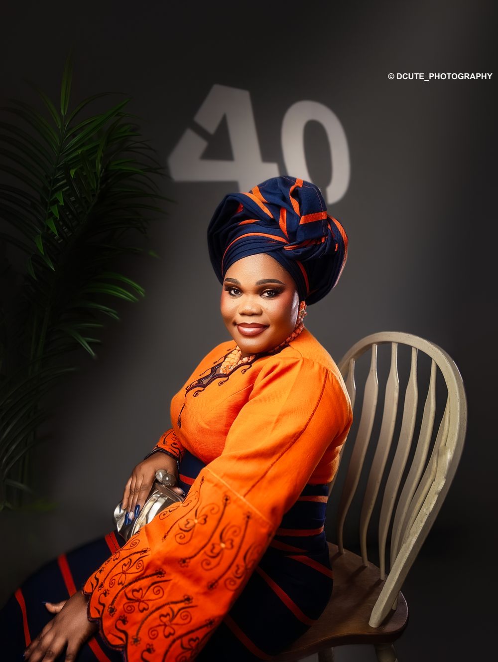 Woman in orange traditional African attire and head wrap poses elegantly at a 40th birthday photoshoot.