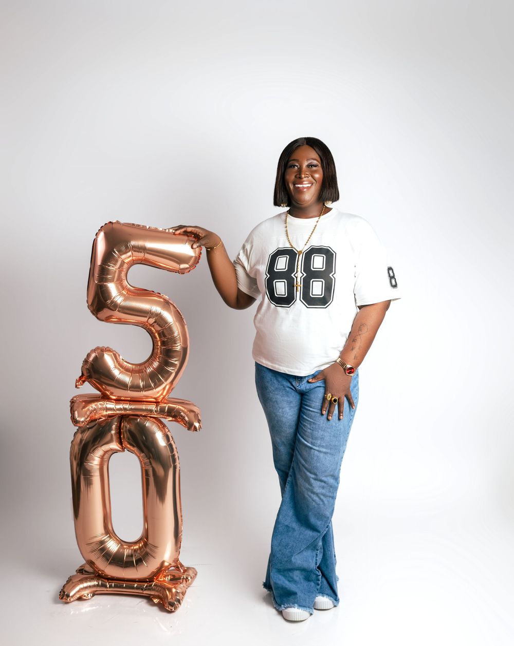 Woman in jersey #88 poses beside rose gold '50' balloons, celebrating a 50th birthday milestone.