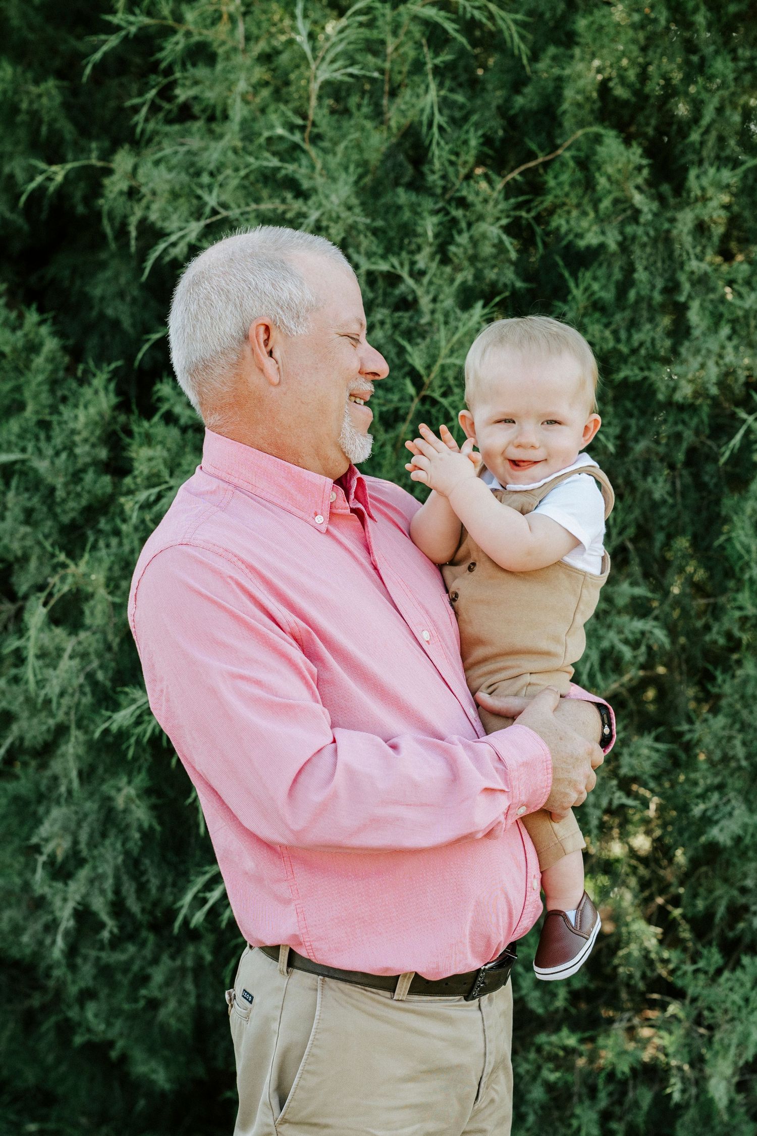 A joyful moment shared between two generations as they smile and laugh together against a backdrop of green foliage.