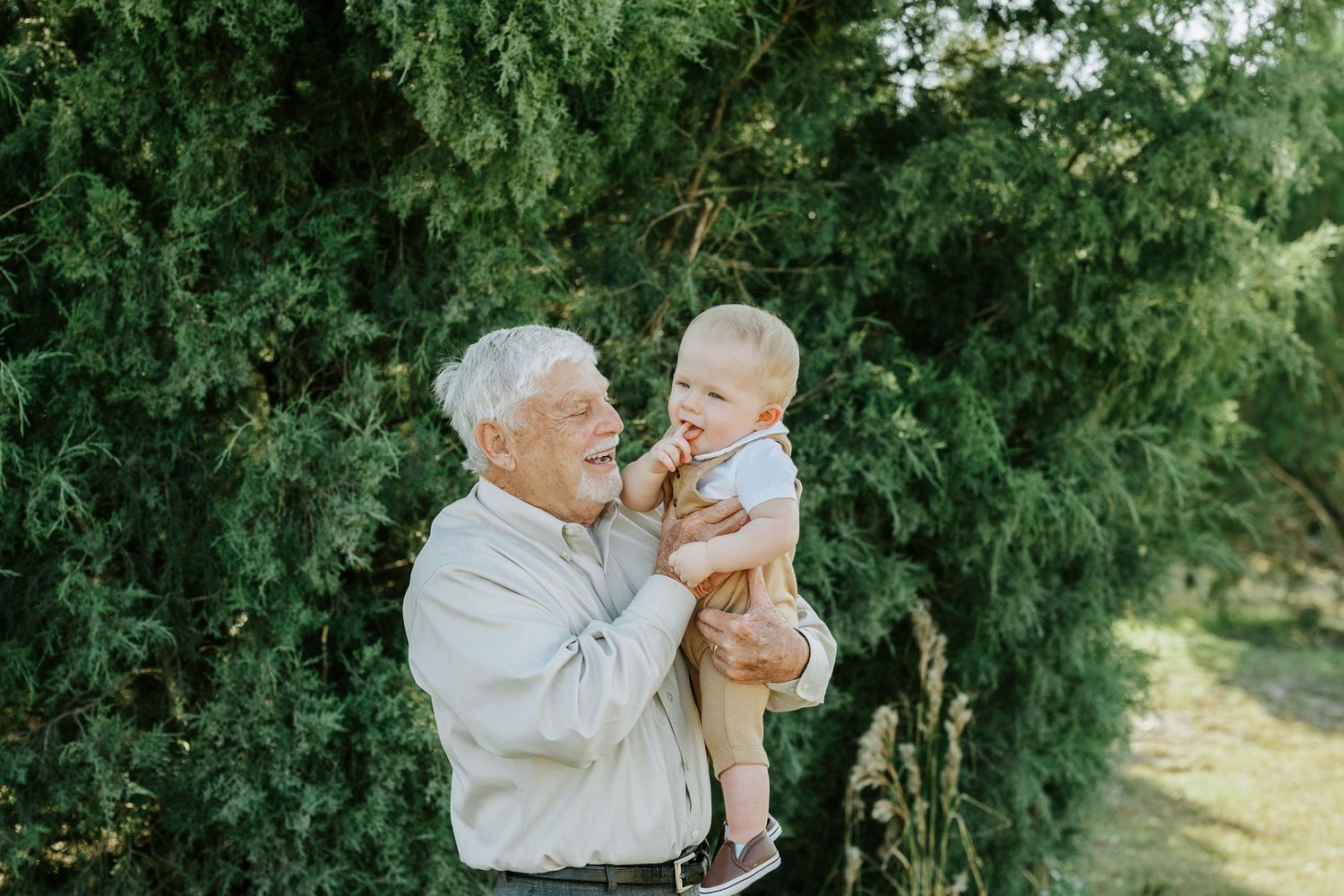 A tender outdoor family moment captured in a lush green garden setting with natural sunlight filtering through trees.