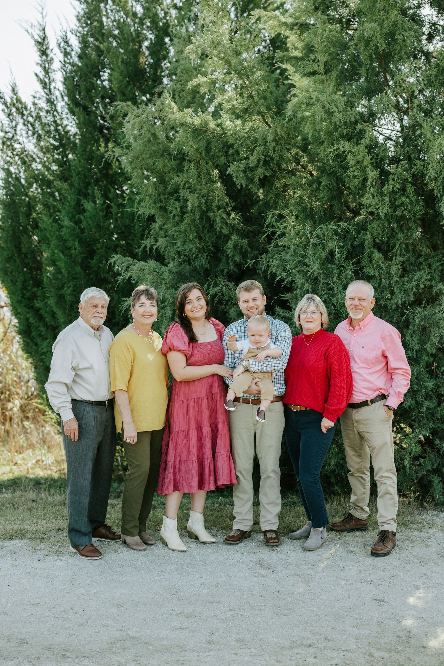 Family members in colorful casual attire stand in a line for a group photo against greenery.