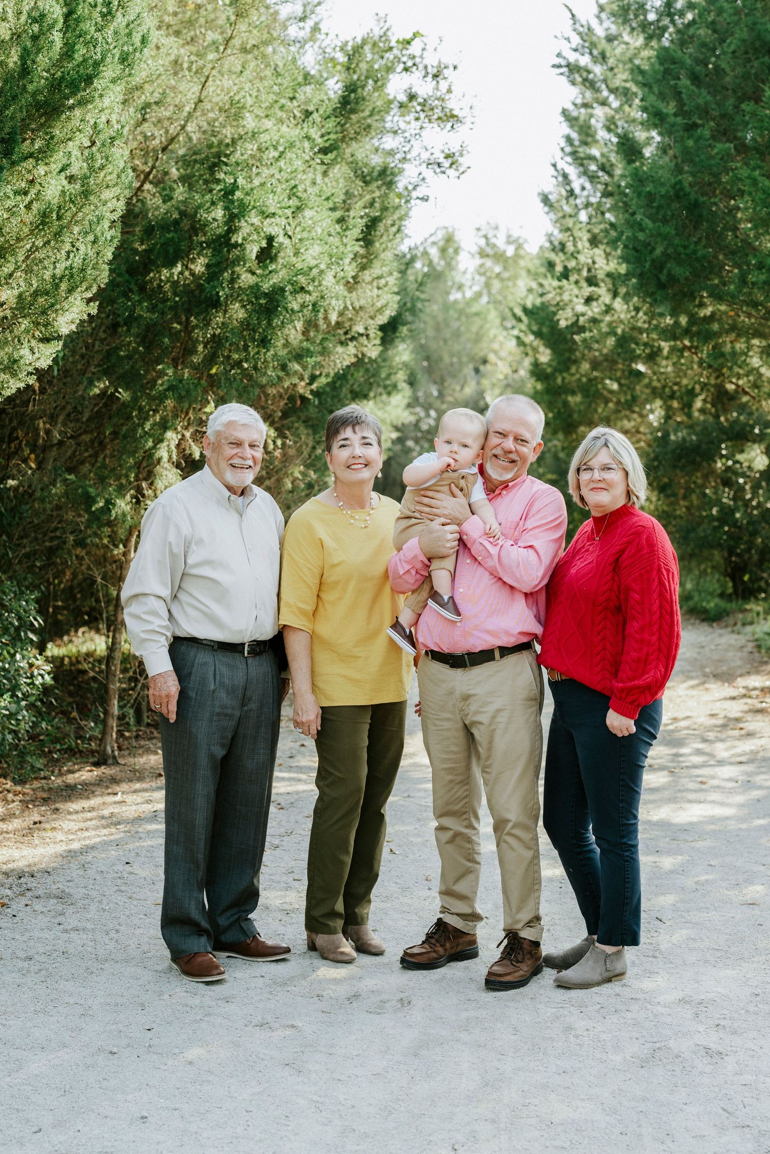 A group of seniors standing together outdoors on a path surrounded by green trees and foliage.