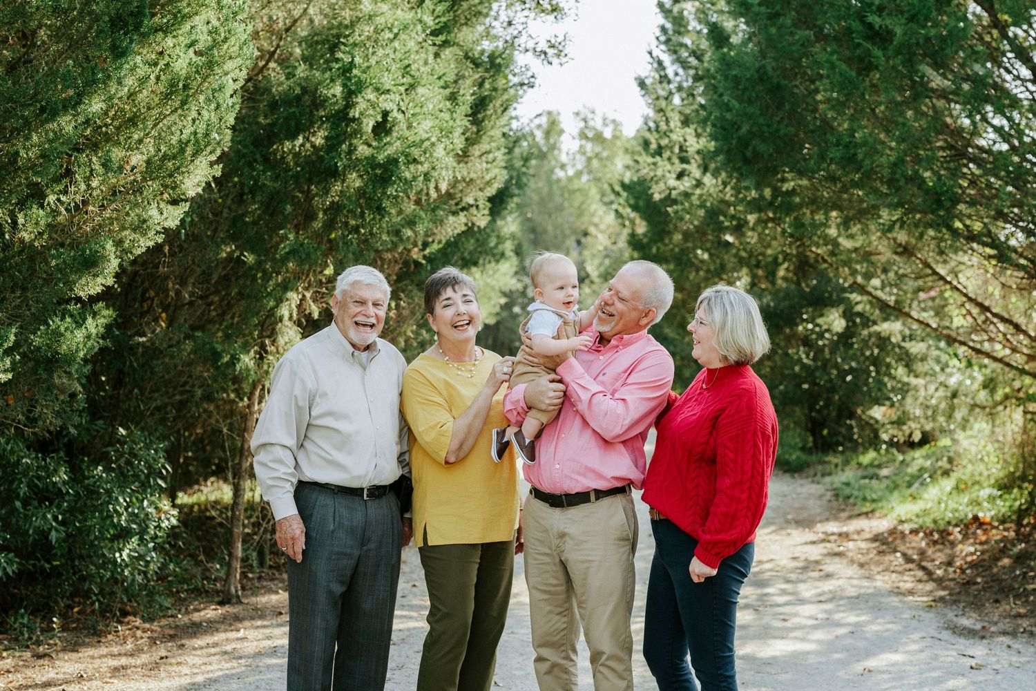Group of people walking and laughing together on a tree-lined path during a sunny afternoon.