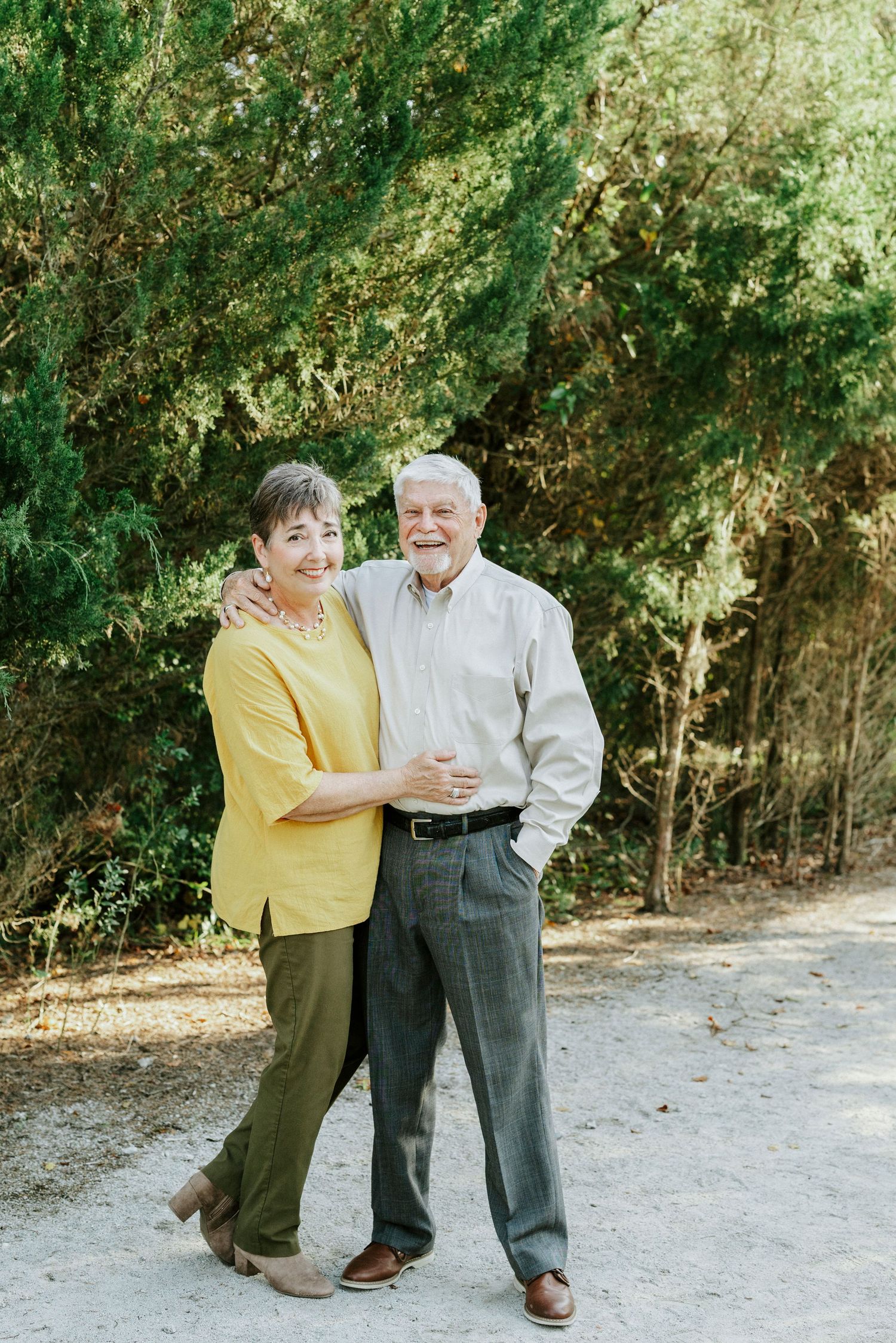 Two people share a tender moment while posing together outdoors near trees.