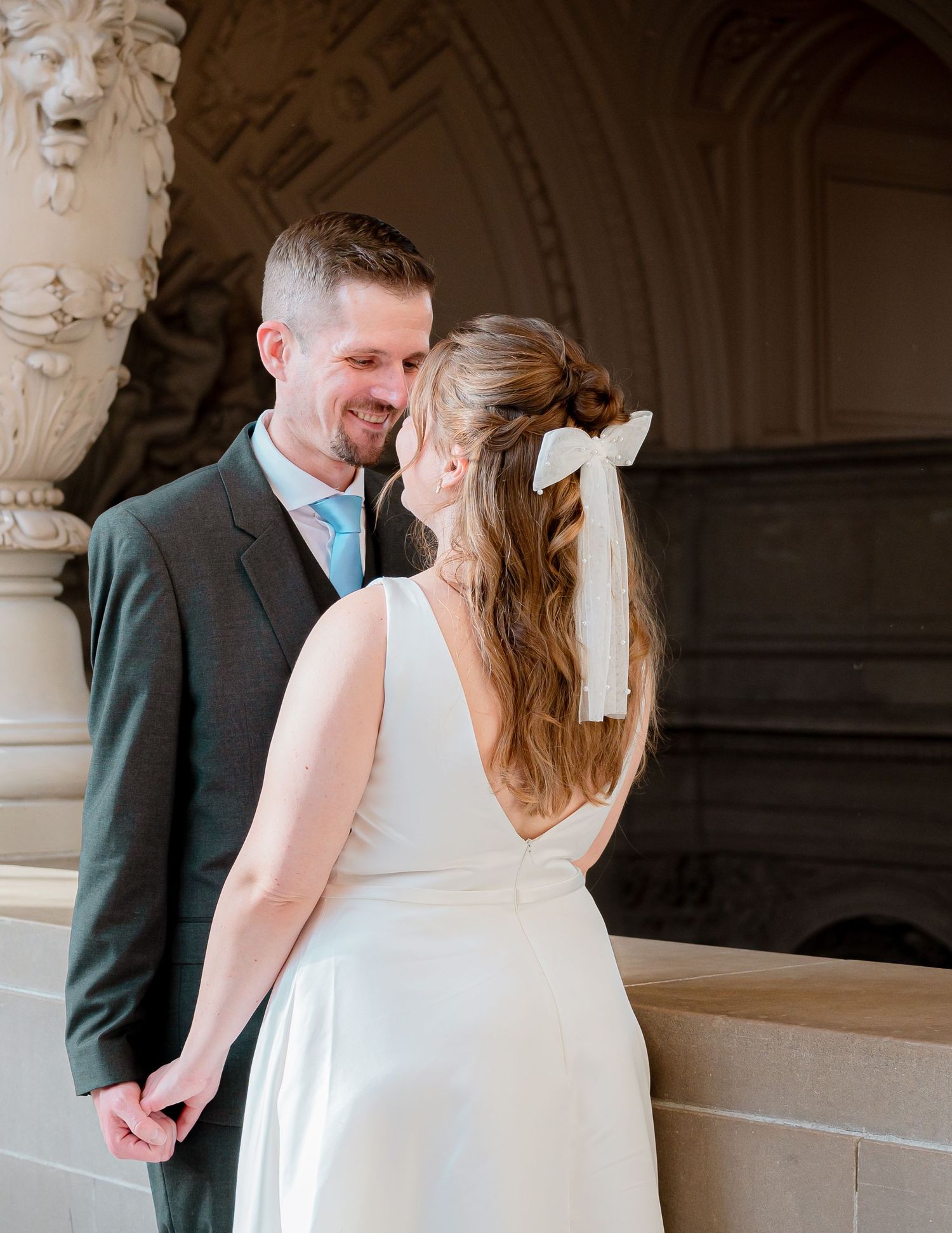 An intimate moment between newlyweds in formal attire against an architectural backdrop.
