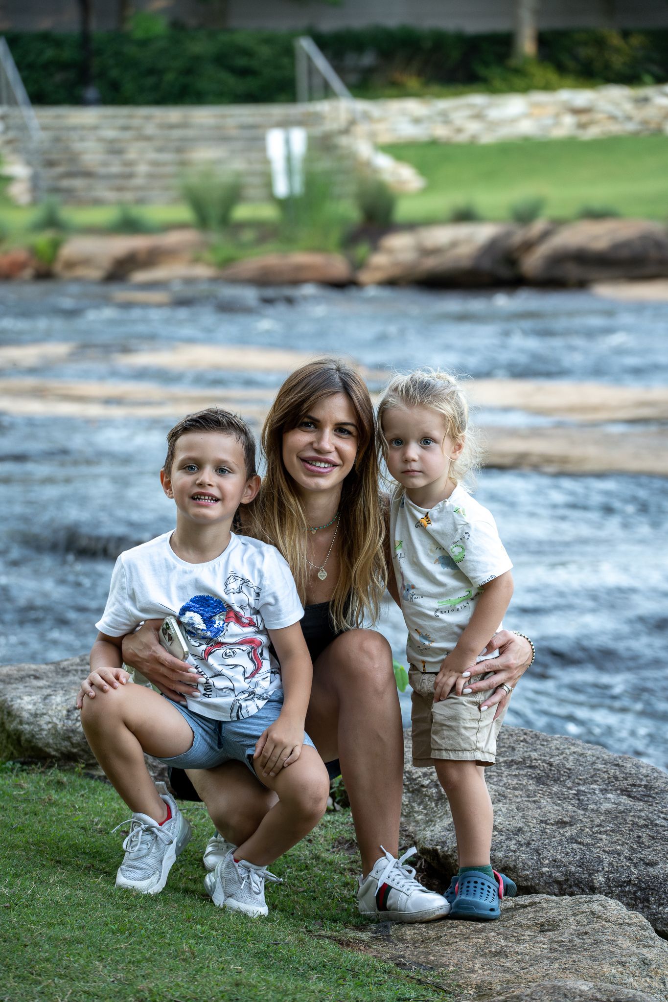 A group sits together on rocks near a flowing river on a sunny summer day.