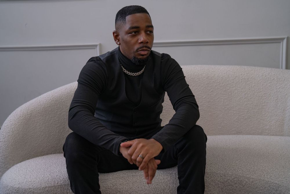 A person in a black sweater sits casually on a light-colored couch in a modern living room setting.