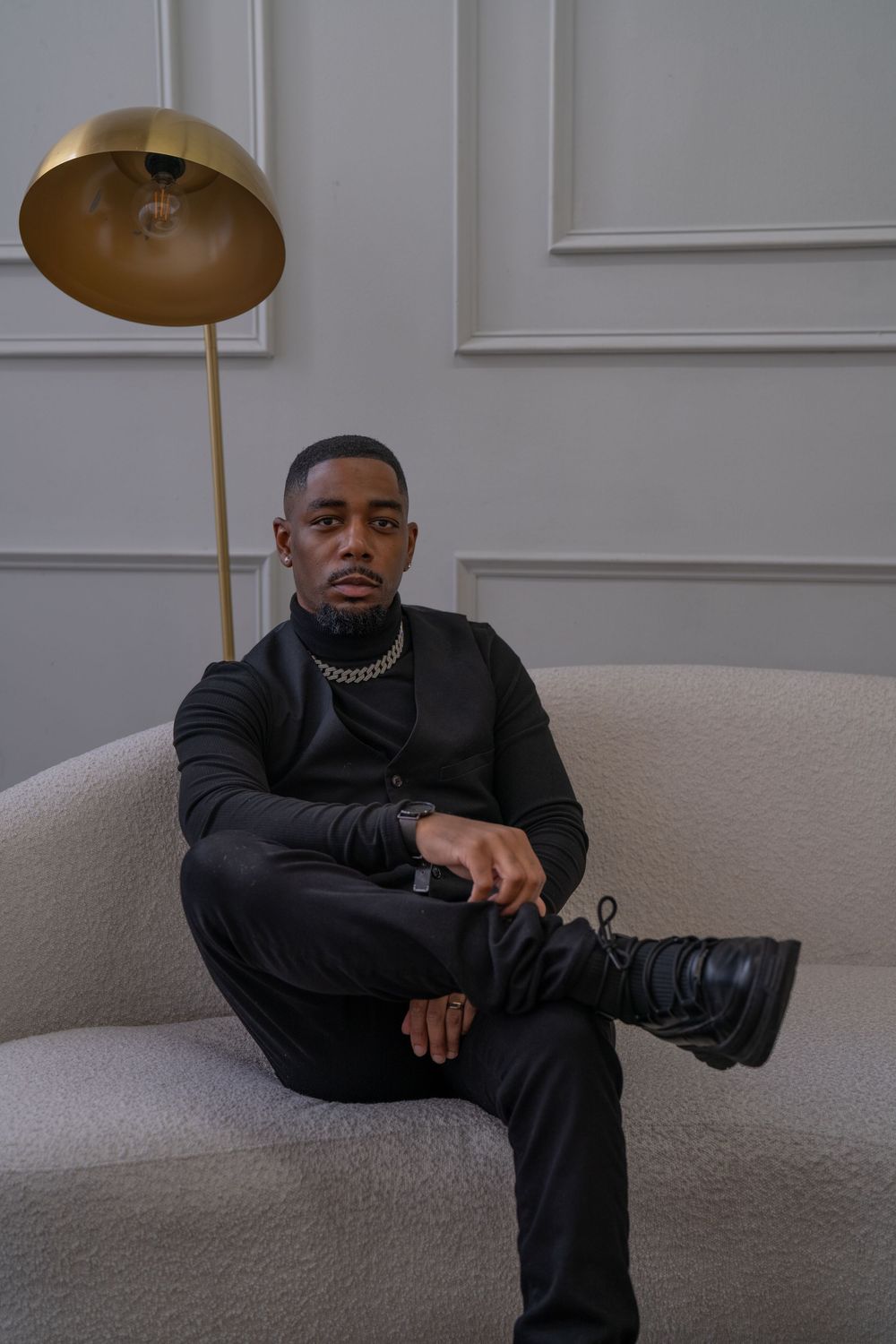 Person in black attire sitting on grey carpet in minimalist white room with cymbal overhead.