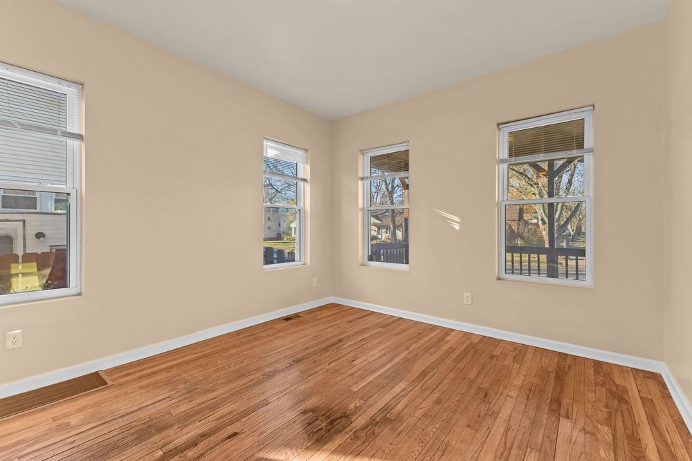Bright empty bedroom with hardwood floors, neutral beige walls, and multiple windows allowing natural light.