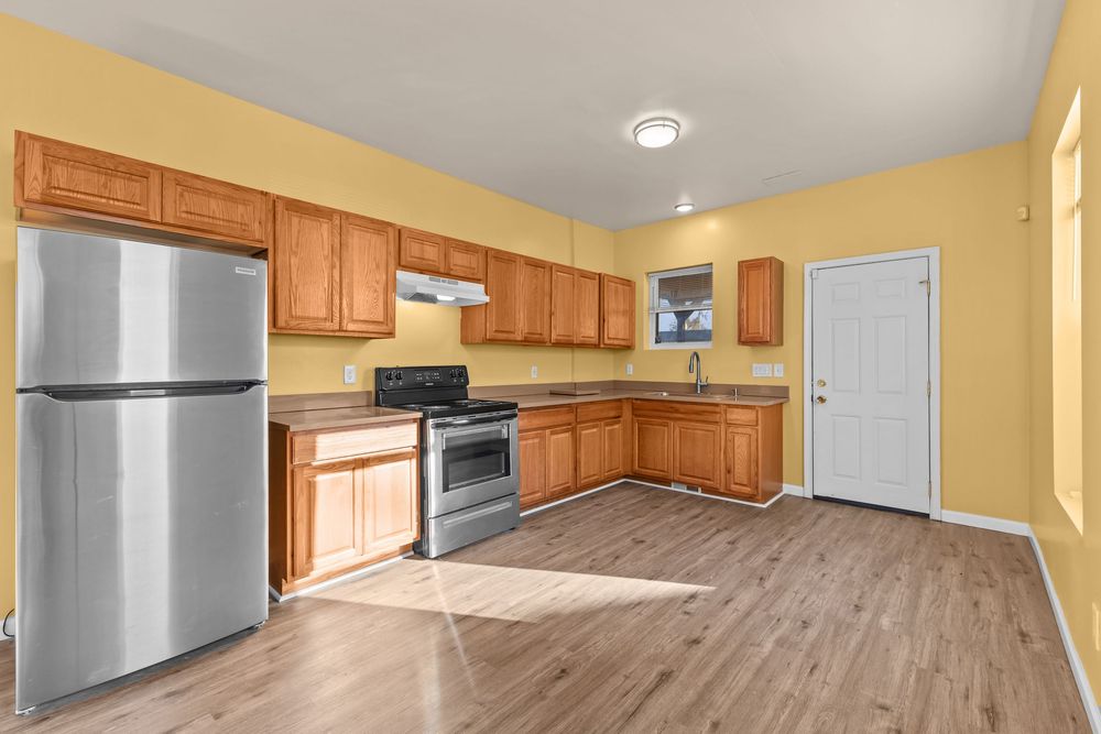Kitchen with honey oak cabinets, stainless steel appliances, and light hardwood floors in a yellow-toned space.