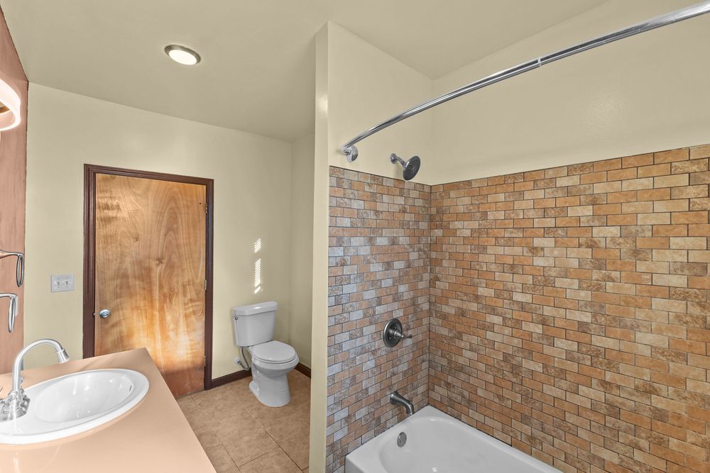 Bathroom with brick-tiled shower-tub combo, toilet, and wood vanity sink in a cozy home.