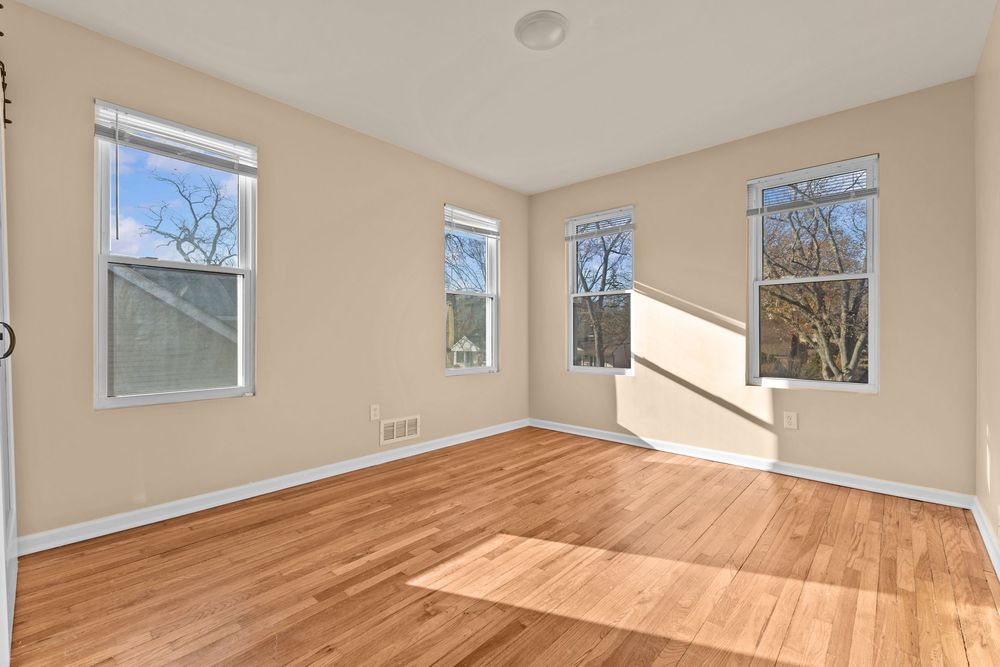 Sunlit empty room with hardwood floors, neutral beige walls, and three large windows.