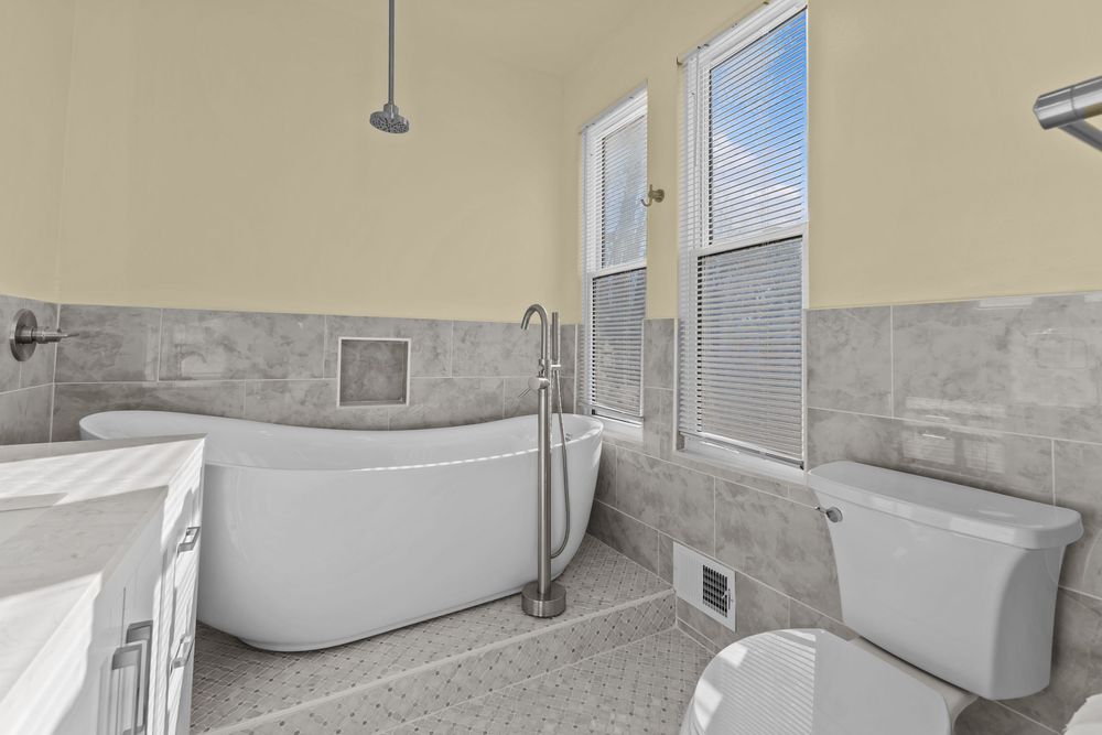 Elegant bathroom with freestanding soaking tub, gray tile wainscoting, and natural light.
