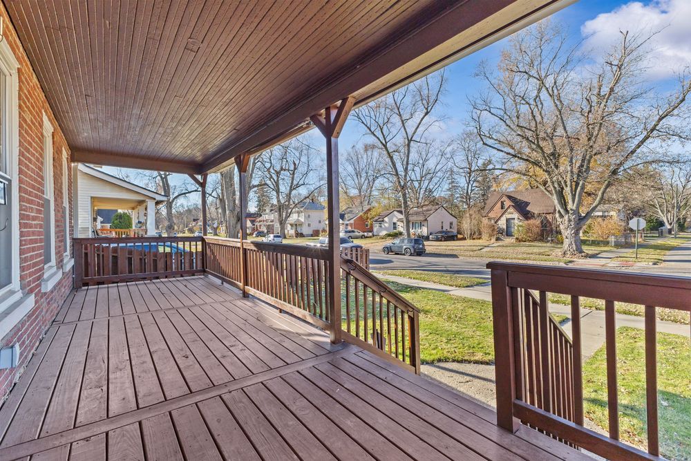 Covered front porch with wood deck, railing, and scenic neighborhood views in daylight.