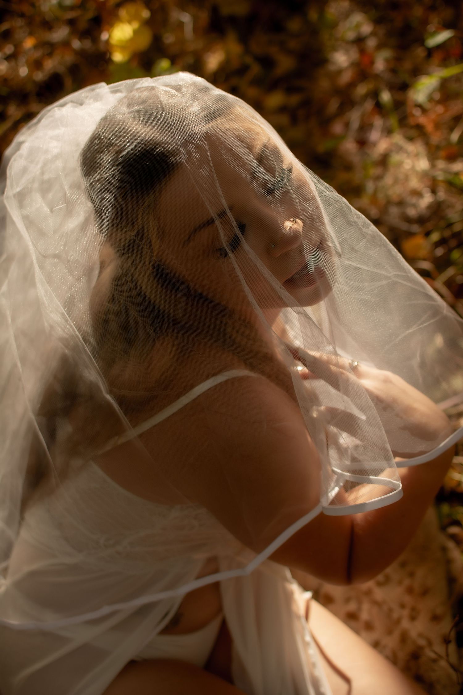 A bride wearing a delicate veil poses in a series of romantic portraits with soft autumn lighting.