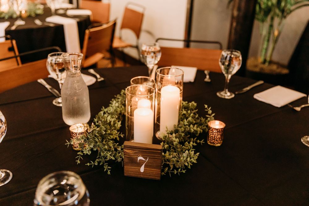 An elegant wedding reception table setting with candlelight, wine glasses and greenery decorations in warm lighting.
