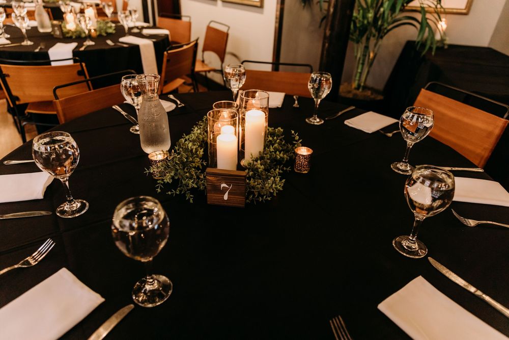 An elegant table setting with black tablecloth, white plates, wine glasses and candlelit centerpiece in a restaurant.