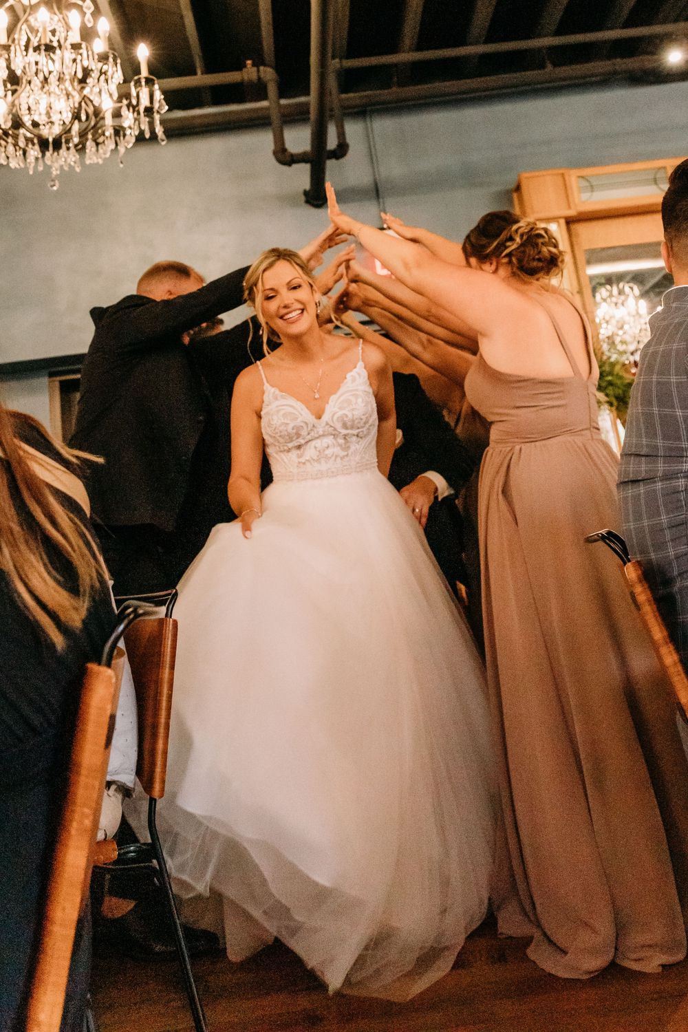 Wedding party members in brown bridesmaid dresses help adjust the bride's flowing white ballgown on the dance floor.