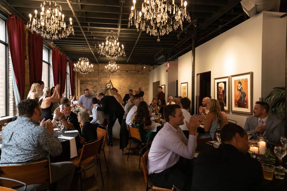 Elegant restaurant dining room with crystal chandeliers, dark wood tables, and framed artwork on cream-colored walls.