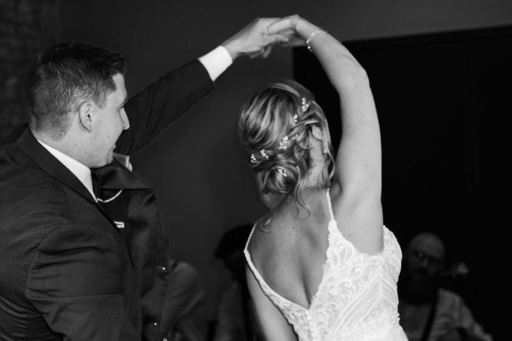 A black and white photo of a couple dancing at their wedding reception with an elegant twirl.