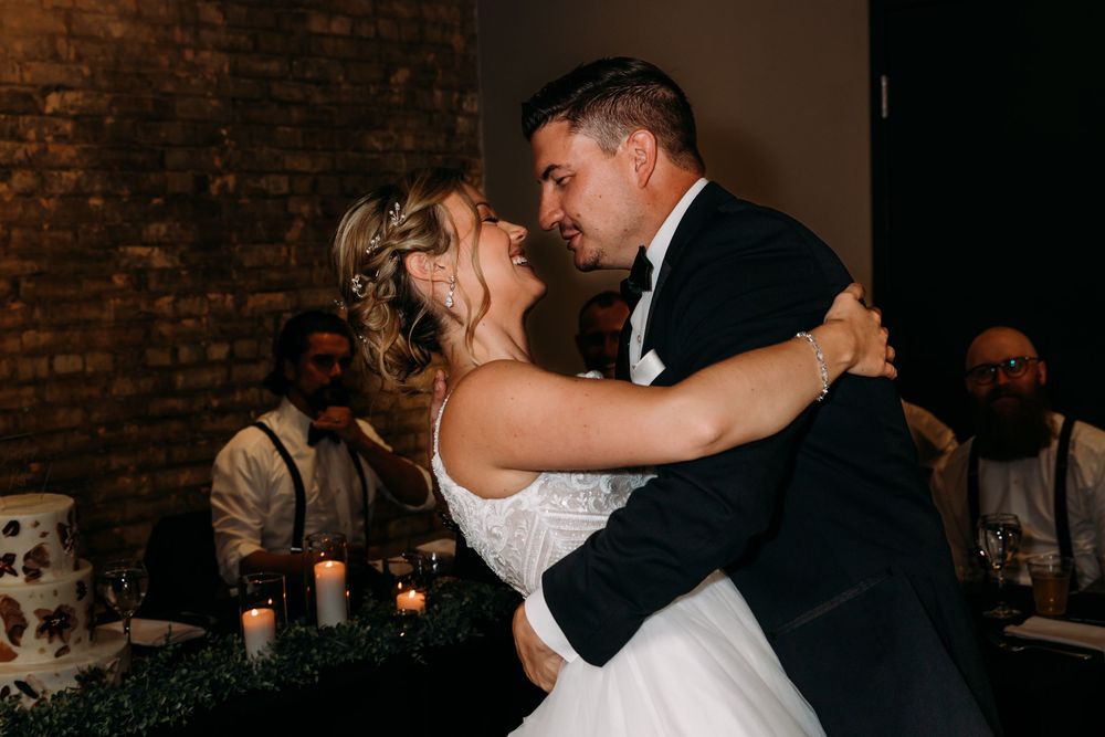 Newlywed couple shares a romantic dance together in an elegant brick-walled venue during their wedding reception.