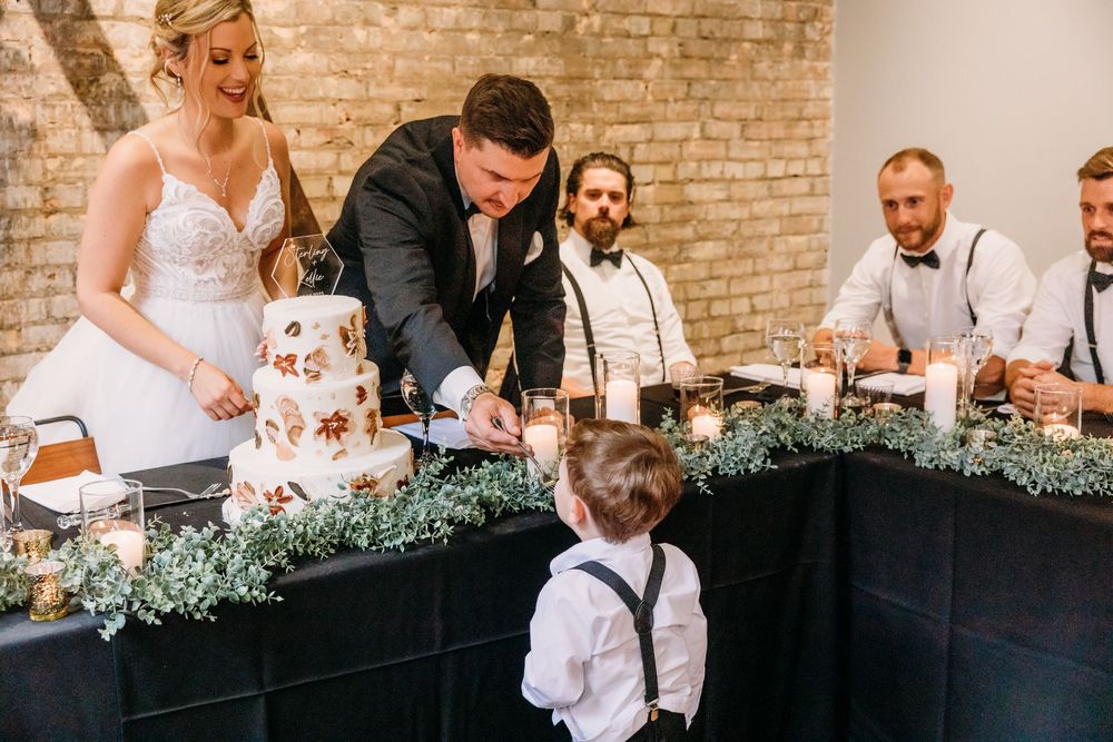 Wedding party gathers around a rustic brick wall venue during reception celebration.
