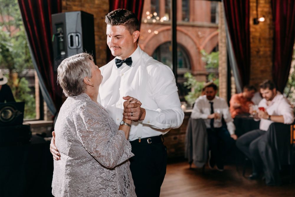 Mother and son share an emotional dance together on wooden floor at wedding reception.