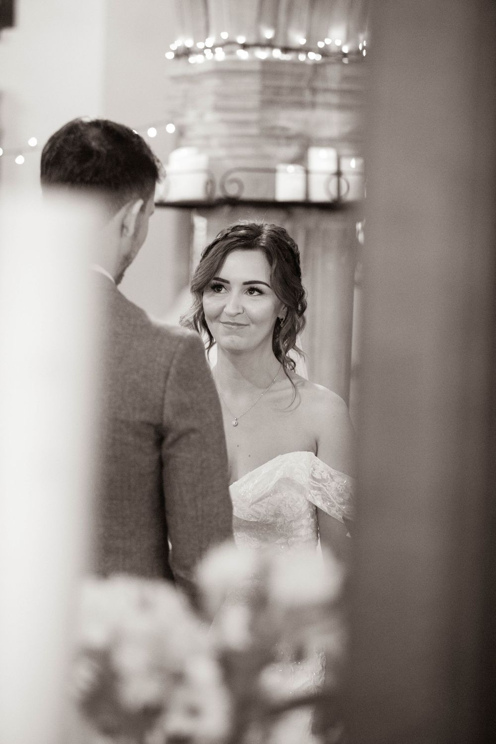 Black and white portrait of smiling bride gazing at groom during wedding ceremony in a church.