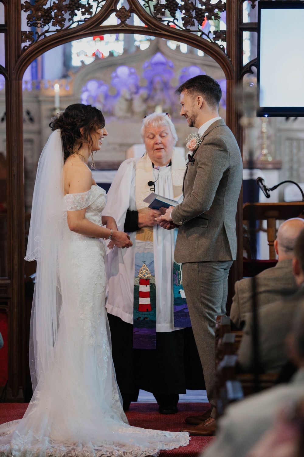 Bride and groom exchanging vows before officiant in a stunning stained glass church interior.