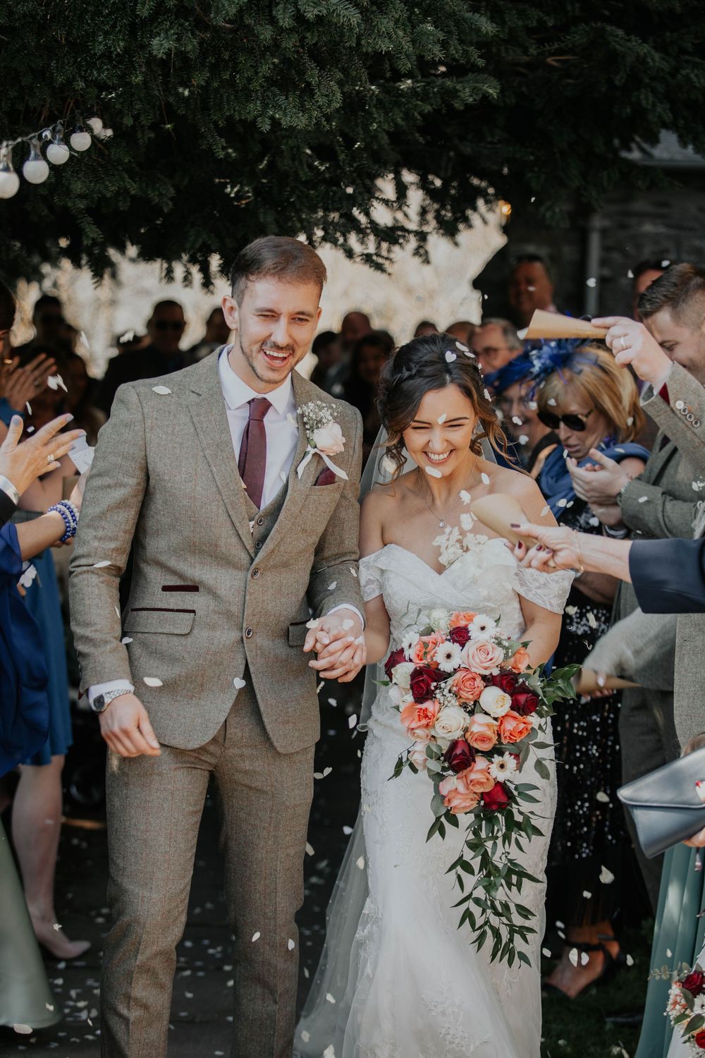 Joyful bride and groom walking through confetti shower surrounded by cheering wedding guests.