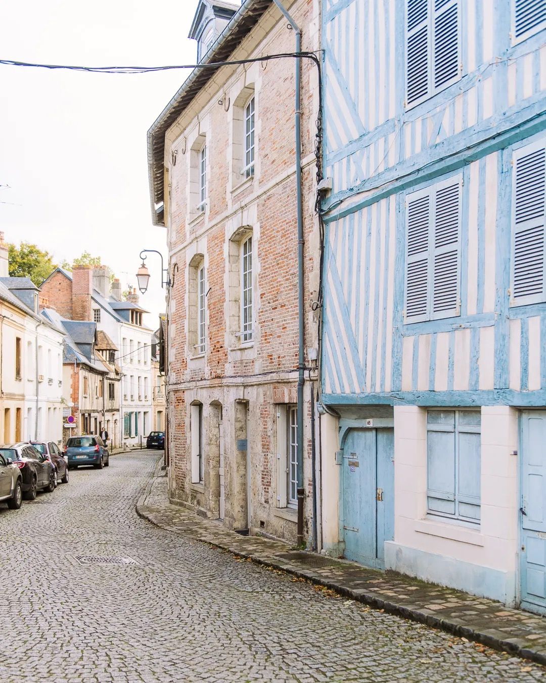 Cobbled street between old French buildings with blue shutters and warm afternoon light.