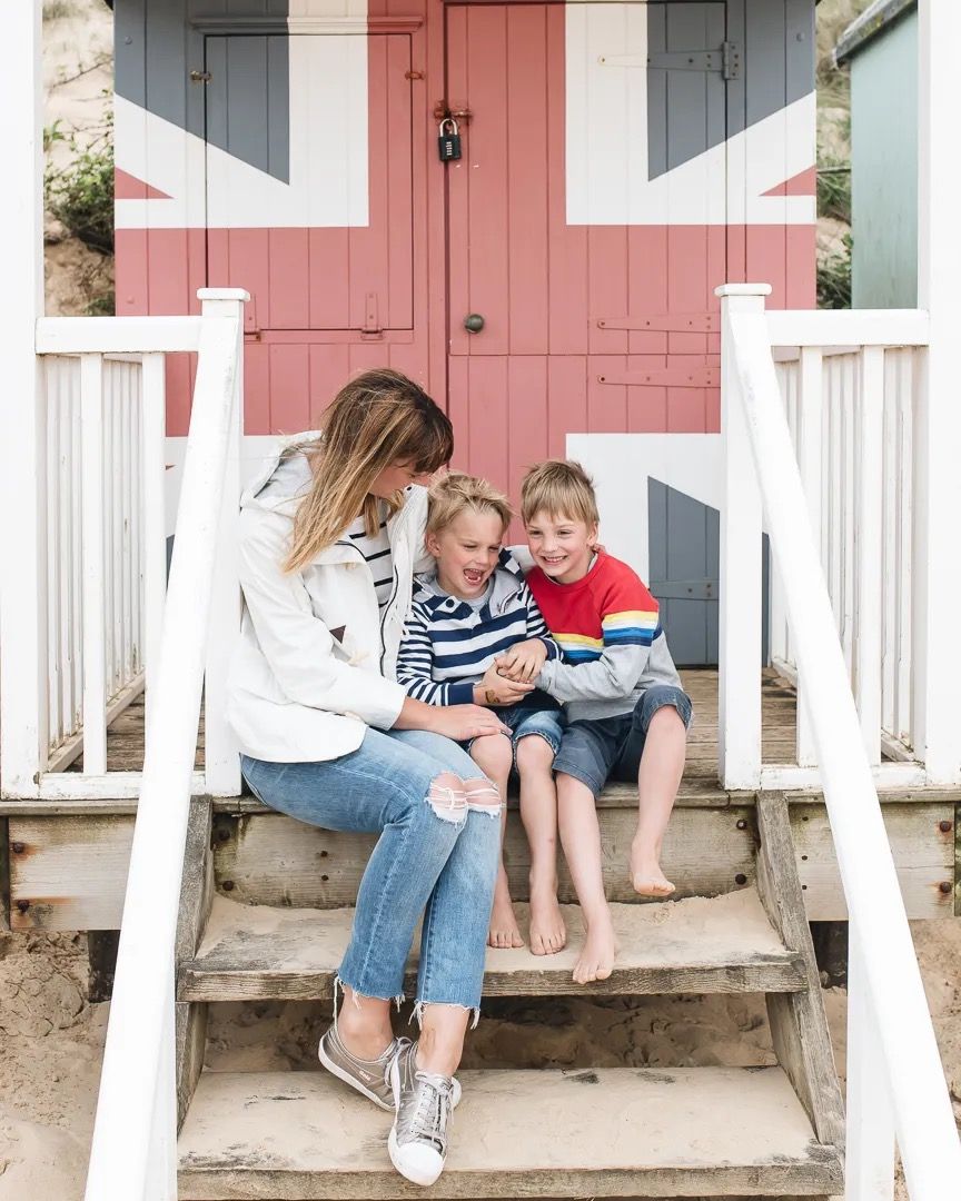 Mum and two children sitting on the white wooden steps of a colourful beach hut.