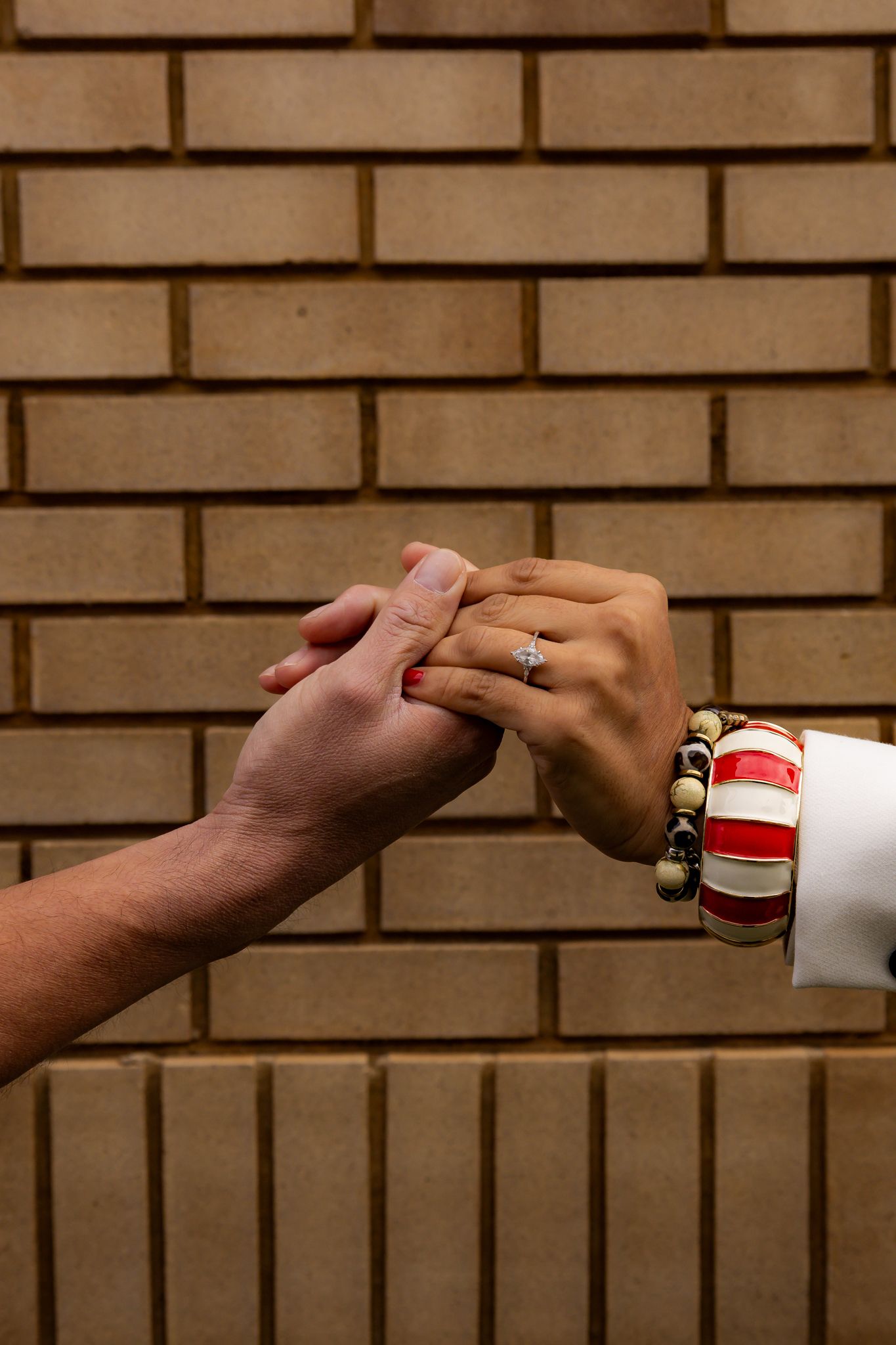 Close-up sequence of hands reaching out to hold each other against a brick wall background.