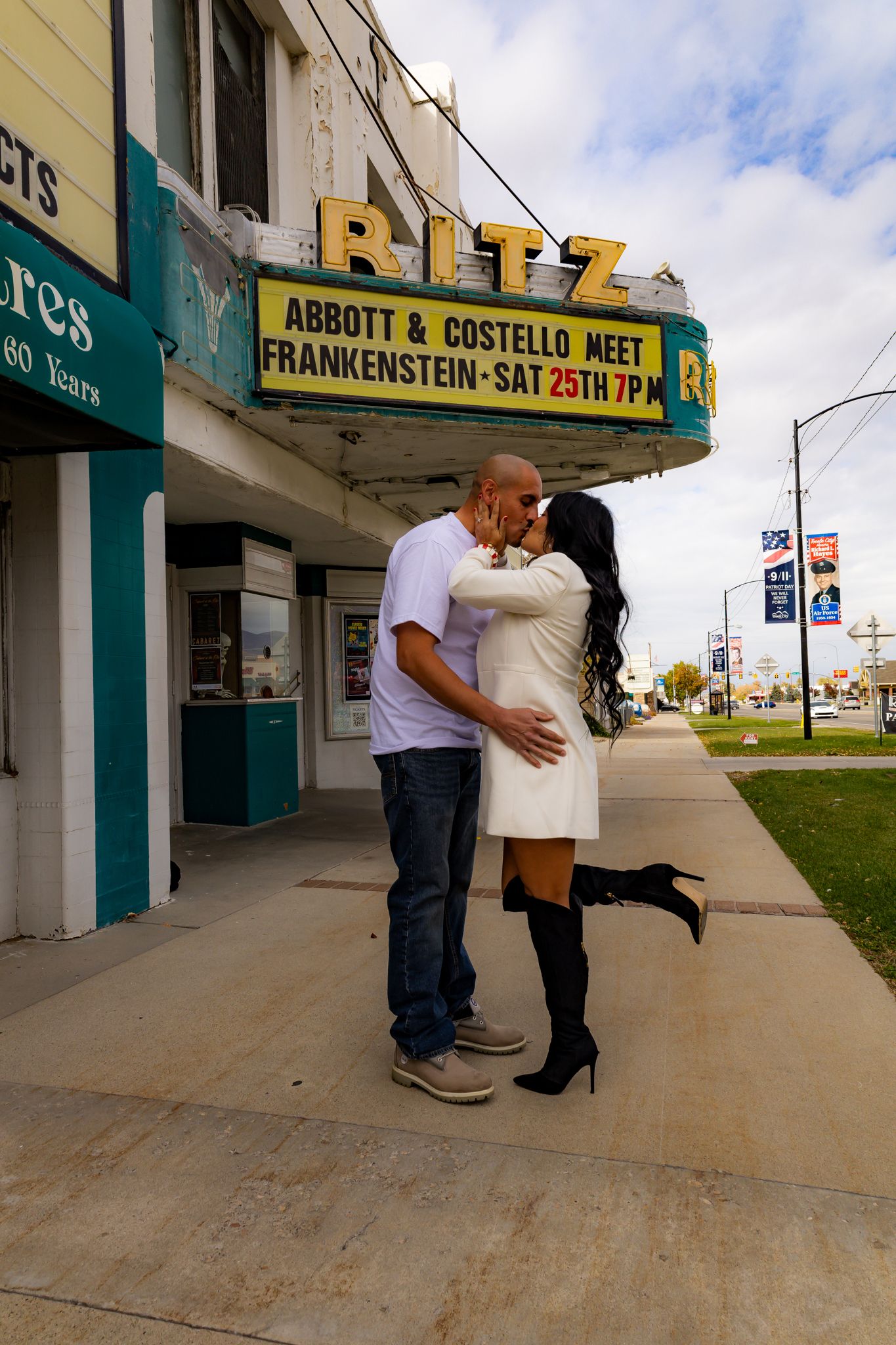 A couple embraces outside a vintage theater with marquee signs visible in the background.